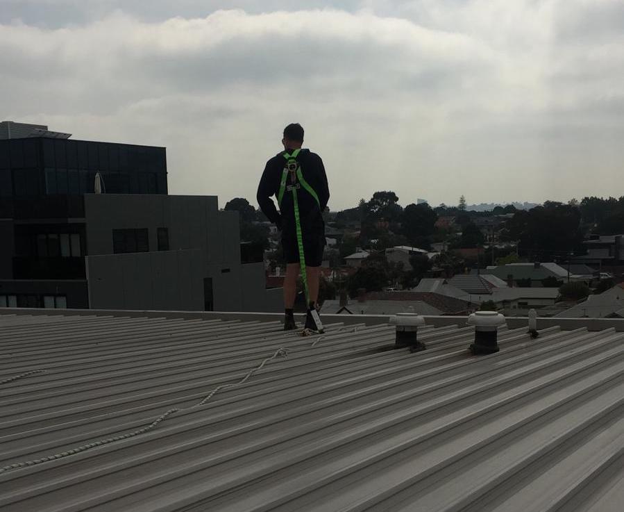 a professional plumber walking along a flat roof, attached by rope